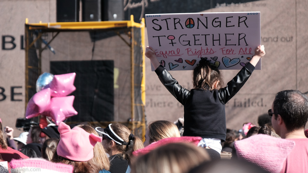 Stronger Together, Equal Rights for All held high above protesters by young girl 